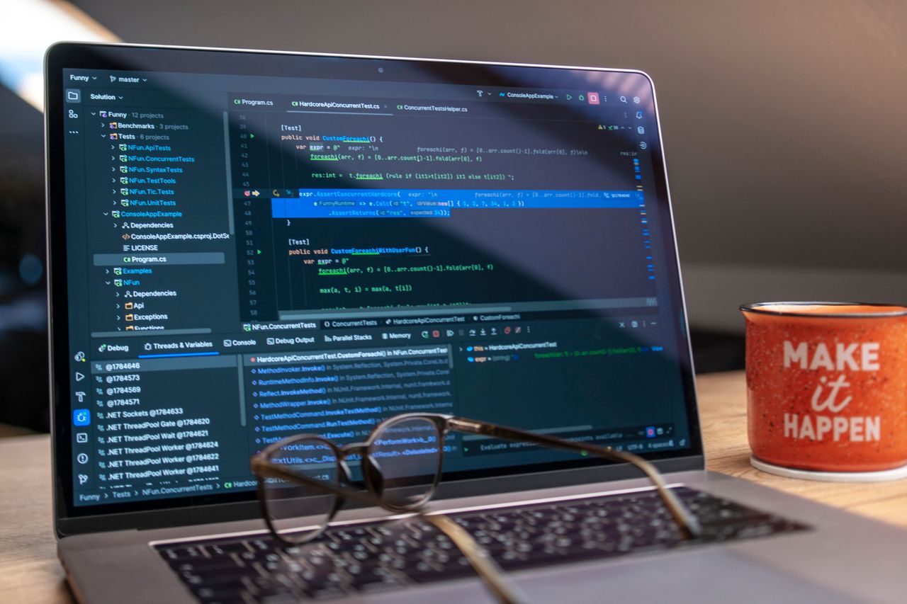 A laptop displaying code editor with a motivational mug that reads 'Make It Happen' on a workspace.